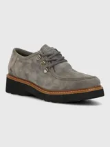Zapato de estilo robusto confeccionado en descarne color gris, con diseño de cordones, ojales metálicos y suela gruesa de goma en color negro con detalle de vira en tono madera.