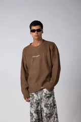 Sweater de cuello redondo en color marrón moka, con diseño de tejido acanalado y calce holgado. Presenta una estampa pequeña en el centro del pecho.