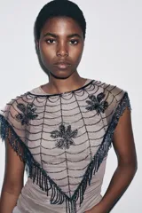 Capa o chal triangular de abalorios azul oscuro, con diseño de telaraña y tres motivos florales o de hojas bordados. El borde inferior tiene flecos largos hechos de abalorios.