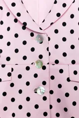Chaqueta corta rosa con estampado de lunares negros, de cuello solapa y manga corta abullonada. Cuenta con falsos bolsillos con solapa en el delantero y cierre frontal con botones.