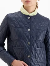 Chaqueta de cuero vacuno azul marino con diseño matelaseado, cuello camisero, cierre frontal con botones metálicos y bolsillos frontales superiores e inferiores.