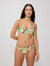 Corpiño de bikini color amarillo claro con estampado tropical de hojas y flores en tonos verde, azul, negro y salmón. Diseño de tirantes finos y escote recto.