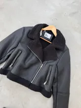 Campera tipo gamulan de cuero sintético negro, con interior y detalles en corderito sintético al tono. Presenta cierre frontal cruzado, bolsillos laterales con cierre y solapas amplias.