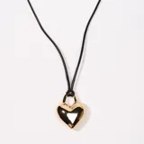 Collar con dije de corazón dorado colgando de un cordón negro.