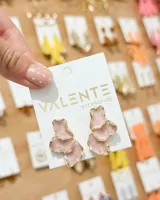 Aros colgantes color rosado pastel con diseño orgánico y borde dorado, compuestos por placas superpuestas.