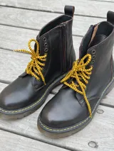 Bota corta de cuero color chocolate, con cordones amarillos y cierre lateral.