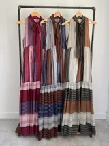 Vestido largo de corte halter en organdí, con estampado de rayas verticales y horizontales en tonos bordó, azul y crudo. Cuenta con un lazo en el cuello y un volado en la parte inferior.