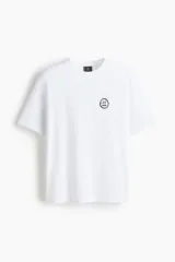 Remera blanca de punto de algodón de peso medio, con cuello redondo ribeteado y hombros caídos. Presenta un pequeño estampado minimalista de un emoji con la boca recta en el pecho.