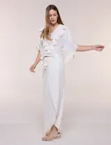 Pantalón palazzo cruzado color blanco con trama en hilo metalizado lurex, cintura elastizada con cordón ajustable con borlas y diseño de piernas anchas con bordes de puntilla y tajo profundo en el frente.