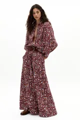 Camisa de lino con estampado floral de margaritas sobre fondo color vino. Presenta cuello camisero clásico, botones frontales de nácar, mangas largas abullonadas y puños con terminación ondulada.