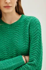 Sweater de punto color verde con diseño de ondas en relieve y sutiles destellos de lentejuelas integradas. Presenta cuello redondo, mangas largas y puños acanalados.