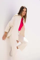 Sobre camisa color crudo, de corte recto, con cuello camisero, cierre frontal con botones y mangas largas con puños abotonados.