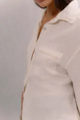 Camisa de lino blanca con cuello tradicional, manga larga, cierre frontal con botones y un bolsillo en el pecho con detalle bordado.
