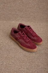 Zapatilla urbana de diseño clásico, color bordó, confeccionada en una combinación de cuero y gamuza. Presenta cordones al tono, suela de goma color caramelo y detalle de marca grabado en dorado en el lateral.
