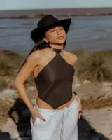 Top de cuero sintético negro con diseño tipo pañuelo, escote halter y cuello rígido metálico integrado. Presenta ajuste lateral mediante tachas metálicas.