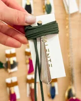 Gargantilla tipo choker con tiento de gamuza verde oscuro y dije triangular plateado. El dije tiene un diseño geométrico con bordes biselados.