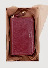 Billetera rectangular de cuero sintético con textura rugosa y acabado brillante, color bordó. Cuenta con cierre perimetral metálico dorado y logo de la marca grabado en el frente.