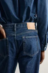 Jeans regular fit de tiro medio, confeccionados en denim de algodón azul oscuro con efecto lavado. Presenta diseño clásico de cinco bolsillos, pierna recta y cierre frontal con cremallera y botón.