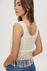 Top sin mangas de crochet color crudo, con escote redondo, diseño calado y terminación con flecos en el ruedo.