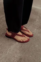Sandalia plana de cuero color rojo, estilo chinela, con tiras finas adornadas con microtachas doradas. Posee tira de sujeción al tobillo con hebilla.