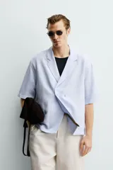 Camisa tipo kimono de corte relaxed fit, color celeste, confeccionada en tejido fluido de viscosa y lino. Presenta cuello con solapas de muesca, manga corta y cierre frontal cruzado con doble botonadura.