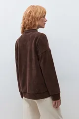 Sweater de pana color marrón con cuello polo y cierre frontal parcial. Presenta un diseño de corte holgado, mangas largas con puños elásticos y textura acanalada.