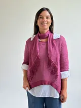 Sweater de punto color magenta con diseño asimétrico, cuello redondo y detalle de encaje bordado en el frente. Incluye una bufanda del mismo tejido y color, y se presenta superpuesto sobre una camisa blanca de algodón.