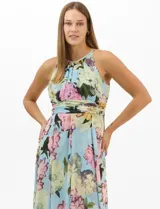 Vestido largo de chifón con estampado floral, cuello halter con pliegues y abertura tipo lágrima. Presenta una cintura drapeada que estiliza la silueta y una falda amplia con capas asimétricas y bajo en picos. Incluye forro interior y cierre invisible en la espalda.