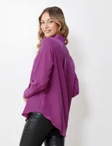 Camisa de satén color violeta, con cuello clásico, cierre frontal con botones, manga larga con puños anchos abotonados y bolsillo aplicado en el pecho.