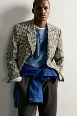 Blazer de corte boxy fit de Zara, confeccionado en tejido con algodón con estampado a cuadros en tonos beige, negro y blanco. Cuenta con cuello de solapas de muesca, manga larga con botones en los puños, bolsillos de vivo en el pecho y de plastrón en la cadera, y cierre frontal con un botón.