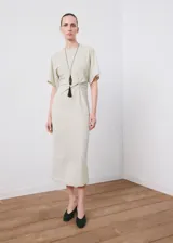 Vestido midi color beige claro, de corte recto, con cuello redondo, mangas cortas holgadas y detalle fruncido en el lateral de la cintura.