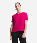 Blusa de tejido plano color fucsia, con cuello redondo, mangas cortas y cierre trasero tipo gota con botón. Presenta detalles de pespuntes en cuello y mangas, y pequeñas aberturas laterales en el ruedo.