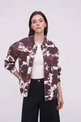 Campera tipo camisa de manga larga con cierre frontal de botones metálicos, bolsillos frontales con solapa y diseño estampado tipo tie-dye en tonos marrones y blancos.