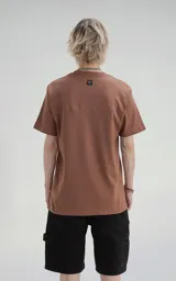 Remera de manga corta y cuello redondo, color marrón (mocca), confeccionada en algodón premium suave. Presenta un calce regular con un recorte distintivo en la espalda.
