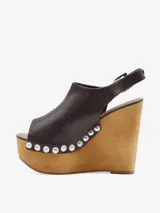 Sandalias de cuero negro con cuña alta de madera y plataforma delantera, detalle de tachas metálicas en los laterales y tira con hebilla en el talón.