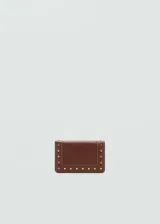 Billetera de tamaño pequeño en color marrón, con diseño de solapa y detalle de tachuelas metálicas doradas en el contorno. Cuenta con compartimento para billetes, múltiples ranuras para tarjetas y bolsillo interior con cierre.