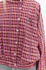 Chaqueta bomber de algodón con estampado a cuadros en tonos azules, amarillos y marrones, cuello alto y cierre frontal descentrado con botones. Cuenta con mangas abullonadas y puños elásticos.