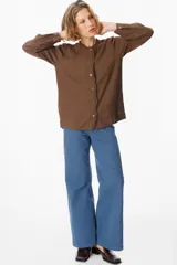 Camisa de manga larga color azul, con cuello mao y detalle de volados en la botonadura frontal. Presenta puños abotonados y un corte recto y fluido.