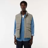 Chaleco acolchado puffer color gris, sin mangas, con cuello alto, cierre frontal de cremallera con solapa de botones a presión y bolsillos laterales amplios.