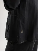 Camisa de lino blanca con diseño de frunces verticales en el frente, cuello camisero y cierre frontal con botones. Presenta mangas largas con puños y un corte recto y holgado.