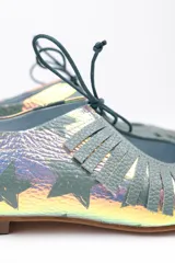 Zapato tipo blucher confeccionado en napa tornasolada con estampado de estrellas en color verde agua. Presenta un adorno artesanal de flecos en napa verde sobre el empeine, cierre con cordones, interior en piel y suela de cuero.