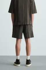 Bermuda de algodón color blanco, de corte relajado (relaxed fit), con cintura elástica ajustable mediante cordón. Posee bolsillos laterales y un bolsillo trasero de plastrón. Presenta un bordado en contraste en la pernera.