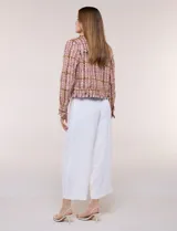 Chaqueta de tweed en tonos rosados, marrones y blancos, con hilos metalizados y lentejuelas brillantes. Presenta cuello camisero, cierre frontal con botones metálicos dorados, bolsillos frontales en el pecho, mangas largas y terminaciones desflecadas.