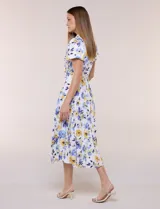 Vestido midi de seda fría blanca con estampado floral en tonos azules y amarillos, escote en V con cuello solapa, mangas cortas, lazo ajustable en la cintura y falda plisada.
