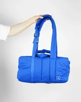 Bolso azul acolchado con doble asa de mano y correa de hombro ajustable.
