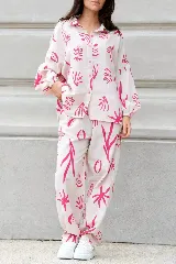 Conjunto de dos piezas compuesto por camisa de corte oversize con mangas largas abullonadas y pantalón de corte holgado con bolsillos laterales. Ambas prendas presentan un estampado botánico en color fucsia sobre fondo crema.