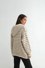 Saco tejido de punto con diseño a rayas horizontales en tonos beige y gris. Presenta capucha con cordones ajustables, cierre frontal con botones de madera, mangas largas y dos bolsillos delanteros.
