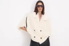 Saco corto de paño color natural con cuello de piel sintética al tono, cierre frontal de doble botonadura y mangas anchas con detalle de línea vertical negra en los laterales.