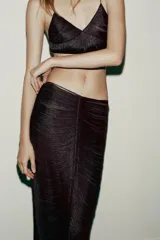 Falda midi de tiro medio, color negro, con aplicación de flecos combinados a tono y bajo asimétrico.