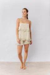 Pijama de algodón estampado con lunares dorados sobre fondo crema. Incluye una musculosa con tirantes finos y volados en el pecho, y un short con elástico en la cintura y volados en el ruedo. Los volados presentan un estampado floral en tonos verdes y crema.